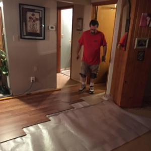 A handyman installing wood laminate flooring in a home, a service provided by Calkins Cabinetry/Handyman's Services in Bentonville, AR.