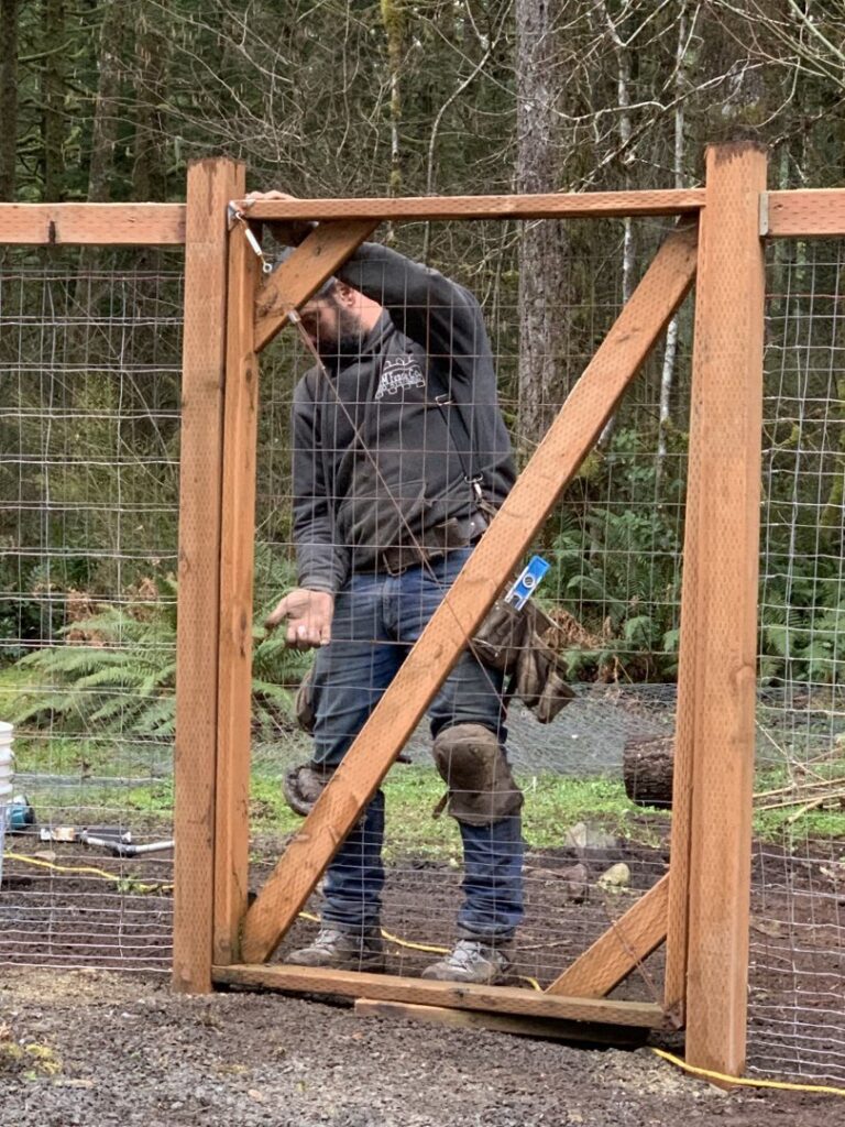 A handyman from J & M Fence Co. installing a wooden gate within a wire mesh fence in Vancouver, WA.