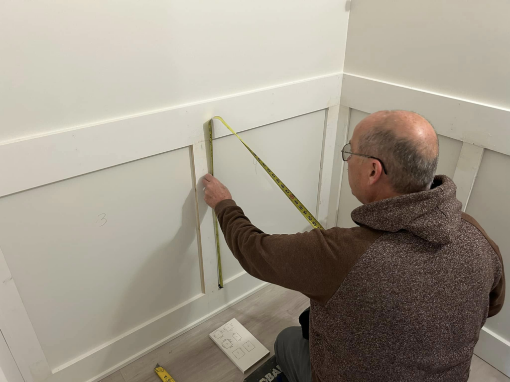 A handyman from Beck & Company Construction measuring a wall with wainscoting in Northport, AL.