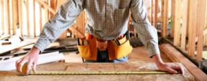 A handyman measuring wood with a tape measure in a construction site, performed by Grassroots Home Specialists in Pueblo, CO