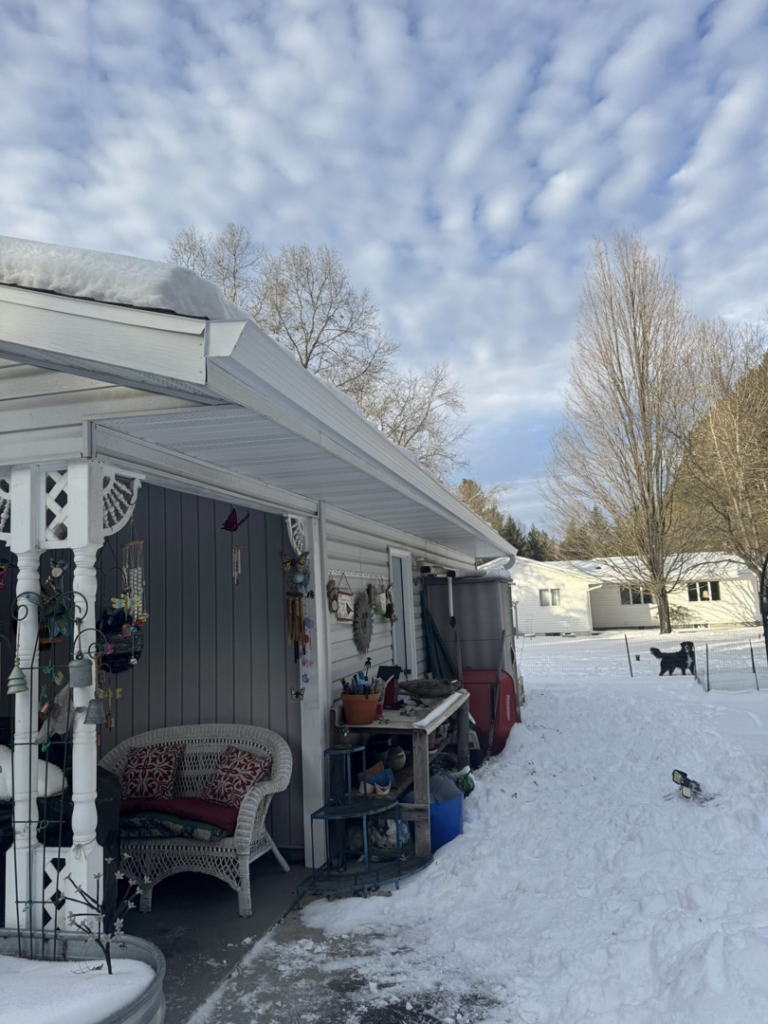 A handyman on a ladder performing gutter maintenance on a house in winter for Timeless Exteriors Inc in Fort Wayne, IN
