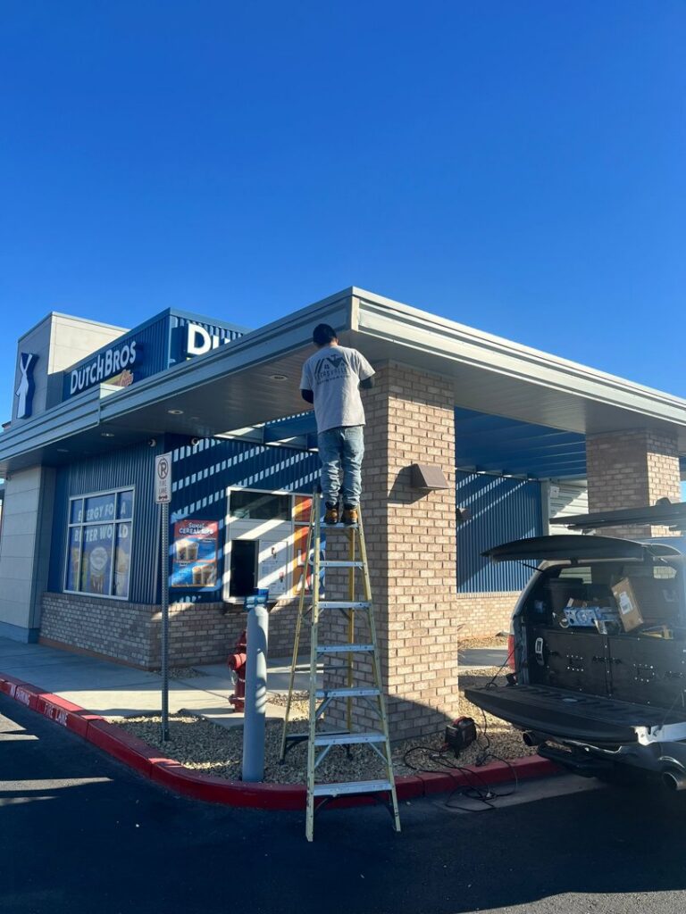 A handyman on a ladder working on the exterior of a commercial building, a service provided by Vegas Handyman Services in Las Vegas, NV.