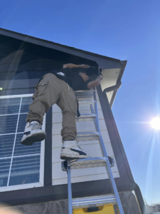 A handyman on a ladder working on the roofline of a house for Ambition Services Llc in Greeley, CO.