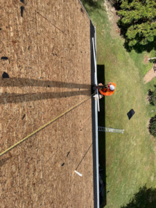 A handyman on a roof deck wearing safety gear and harness, performing work for New American General Construction INC in Richmond, VA.