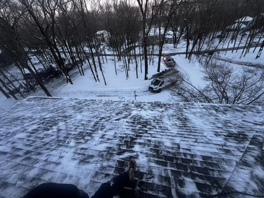 A handyman on a snowy roof with a work van parked below, performing winter roof services for BETHO Construction INC in Milford, MA.