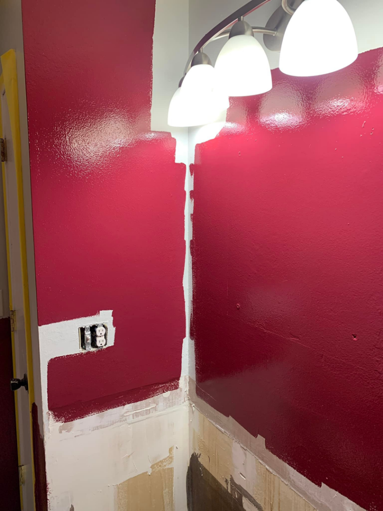 A handyman actively painting a bathroom wall with red paint, demonstrating a service by All-Pro Handyman in Bellevue, NE.
