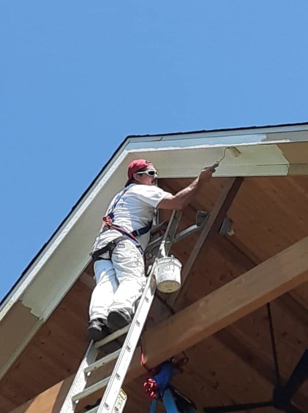 A handyman from Brown & Sons Restoration painting exterior trim on a house in Denver, CO.