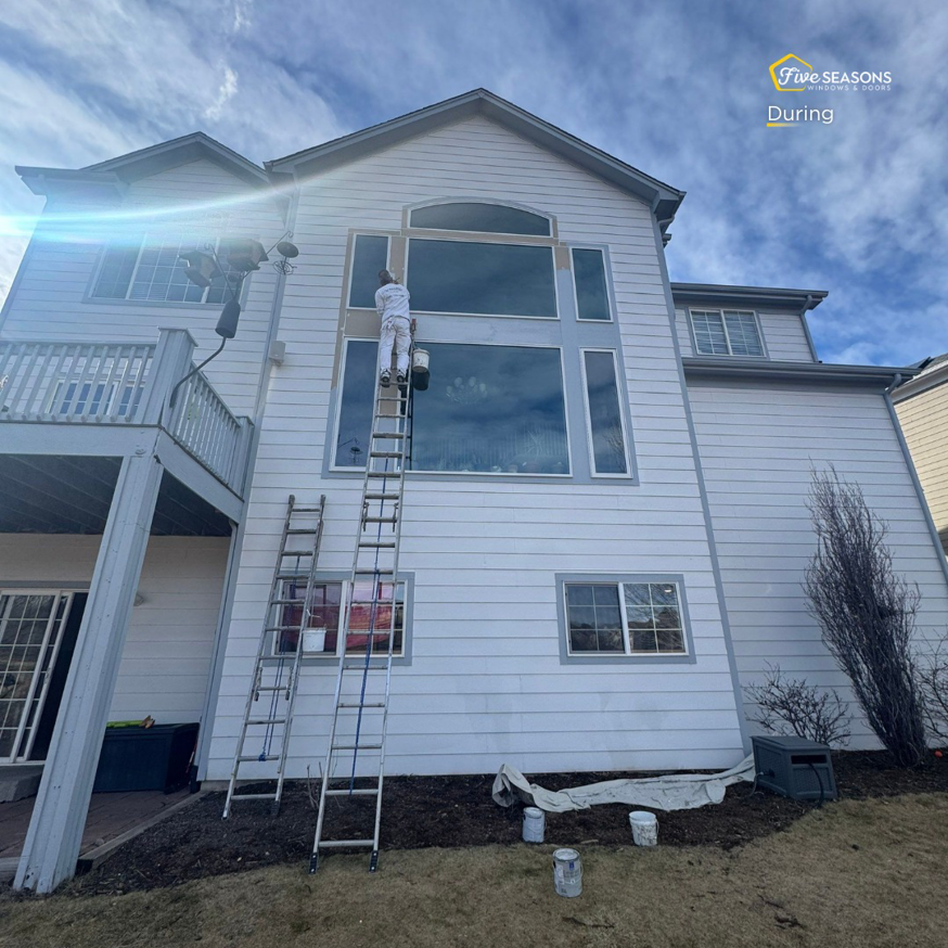 A handyman painting exterior window trim on a house, provided by Five Seasons Windows and Doors in Denver, CO.