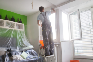 A handyman painting an interior room while standing on a ladder for Skilled Hands Residential Contracting in Covington, KY.