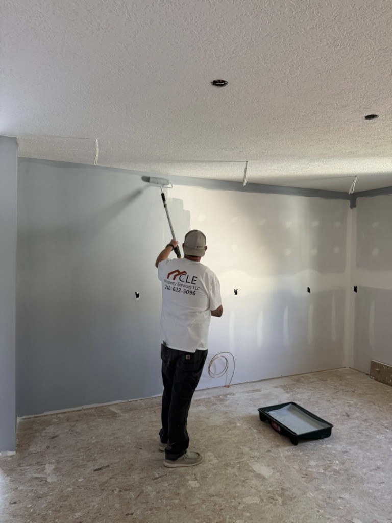 A handyman from CLE Property Services LLC painting an interior wall with a roller in Cleveland, OH.