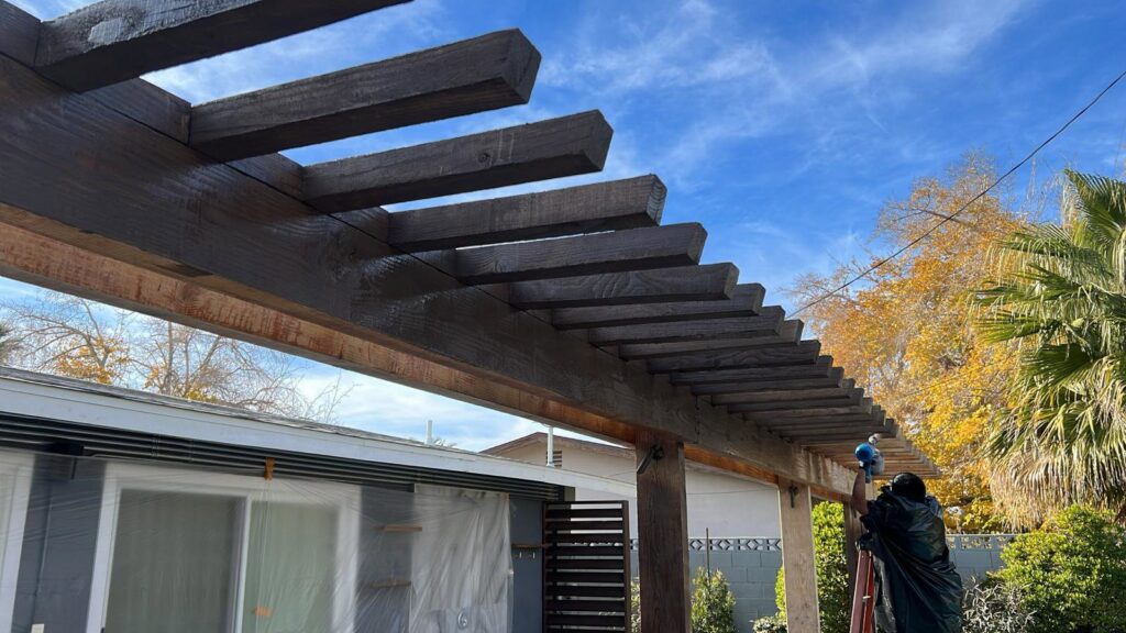 A handyman painting or staining an outdoor wooden pergola structure, a service offered by Vegas Handyman Services in Las Vegas, NV.