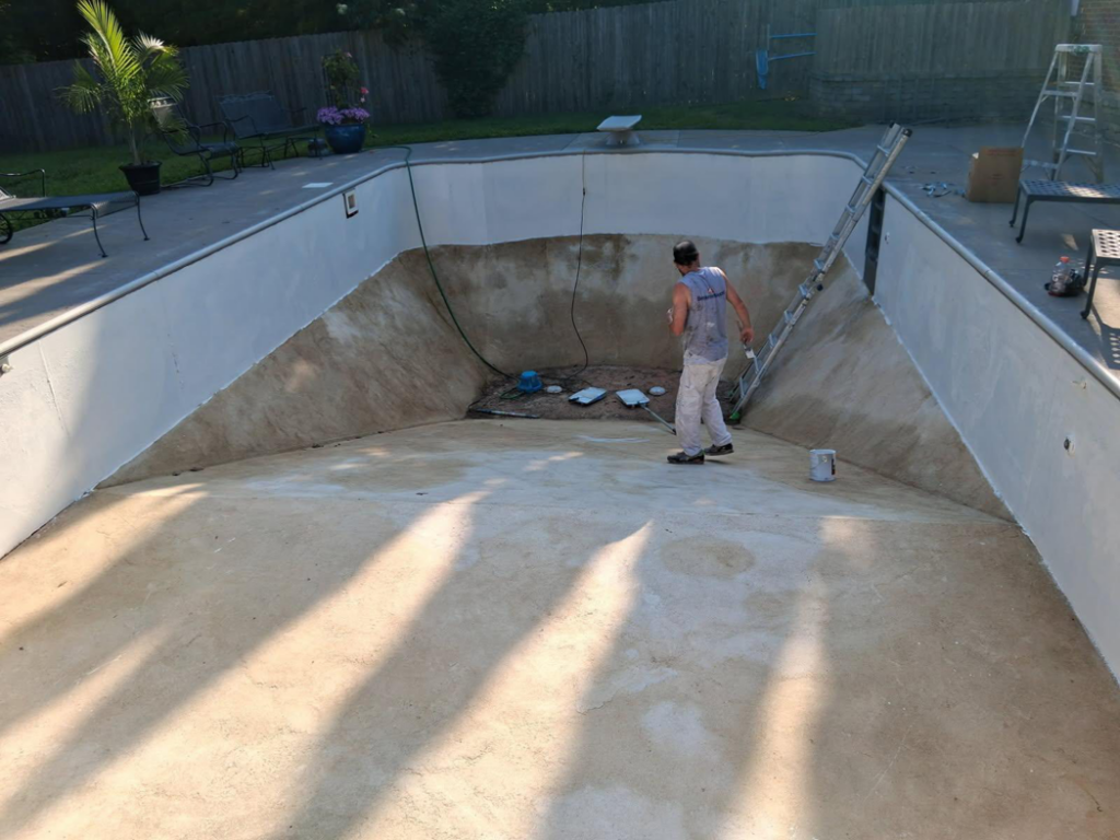 A handyman painting and resurfacing an empty swimming pool for Premier Power Washing in East Islip, NY
