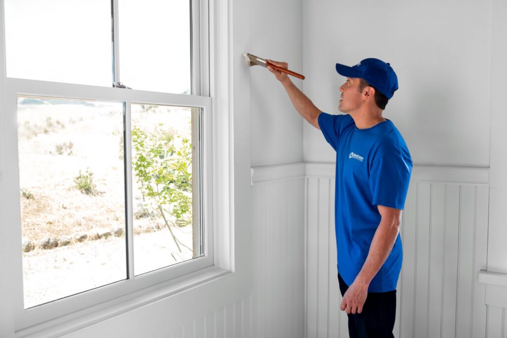 A Handyman Connection of Wichita East professional paints a wall next to a window in Wichita, KS.