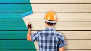 A handyman in a hard hat painting a wooden wall with a roller for A 'n' G Residential in Amsterdam, NY.