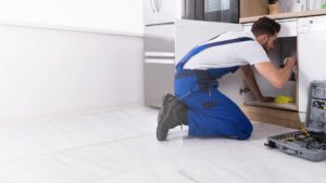 A handyman performing plumbing repair under a kitchen sink for Priority One Home Repair LLC in Glendale, AZ
