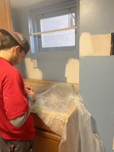 A handyman preparing a wall for painting or renovation above a counter for Professional Restoration in Jersey City, NJ