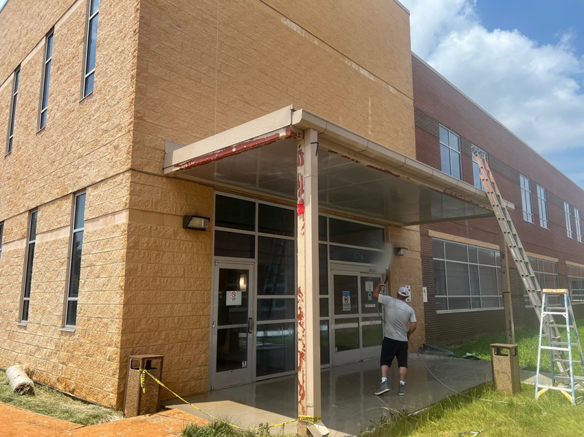 A handyman pressure washing the entrance and awning of a commercial building for Selk Solutions in Crossville, TN.