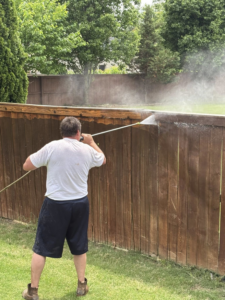 A handyman actively pressure washing a wooden fence for Precise Drain & Home Services in Springdale, AR.