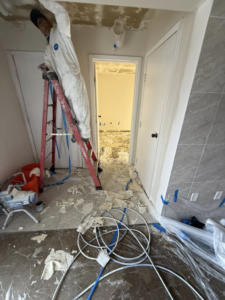 A handyman on a ladder actively removing a popcorn ceiling in a home serviced by AM Remodels LLC in Denver, CO.