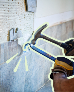 A handyman removing old wall tiles with a hammer and pry bar for Pjai Projects in Nashville, TN