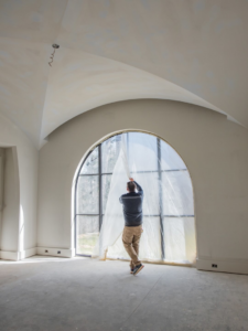 A handyman removing protective plastic from a large arched window for South Haven Builders in Athens, GA