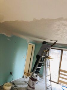 A handyman on a ladder repairing a ceiling with plaster or drywall mud for Drywall Paint Plus in Worcester, MA.