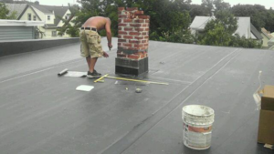 A handyman working on repairing a brick chimney on a flat roof, a service by Camelot Development in Bridgeport, CT.