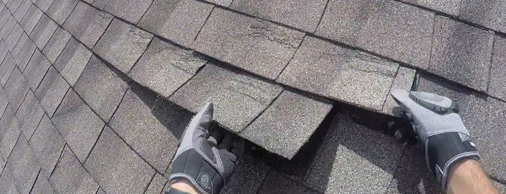 A handyman from Castle Contracting Group in Cincinnati, OH, inspecting or repairing a damaged asphalt roof shingle.