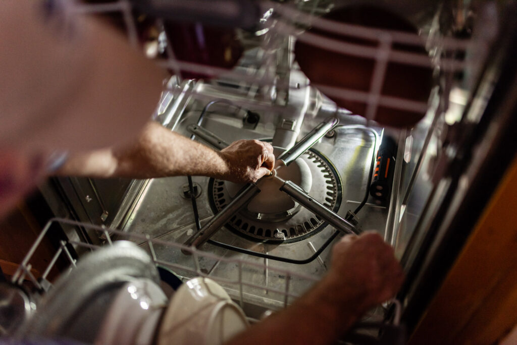 A handyman performing a repair inside a dishwasher, working on internal components for Larry's Appliance Repair in California, MO.