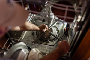 A handyman performing a repair inside a dishwasher, working on internal components for Larry's Appliance Repair in California, MO.