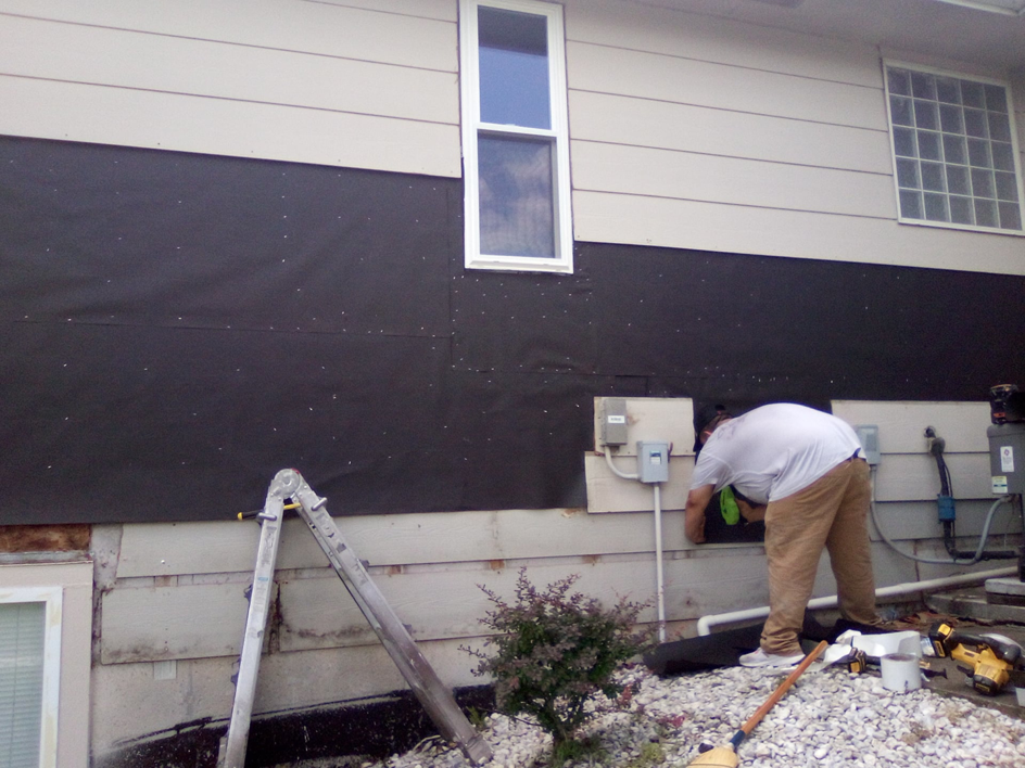 A handyman repairing exterior siding and foundation on a house by Picasso Handyman Painters in Wichita, KS.