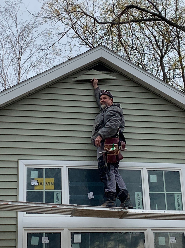 A handyman from Geoff Lafayette Builder, LLC repairing a gable vent on a house in Madison, WI.