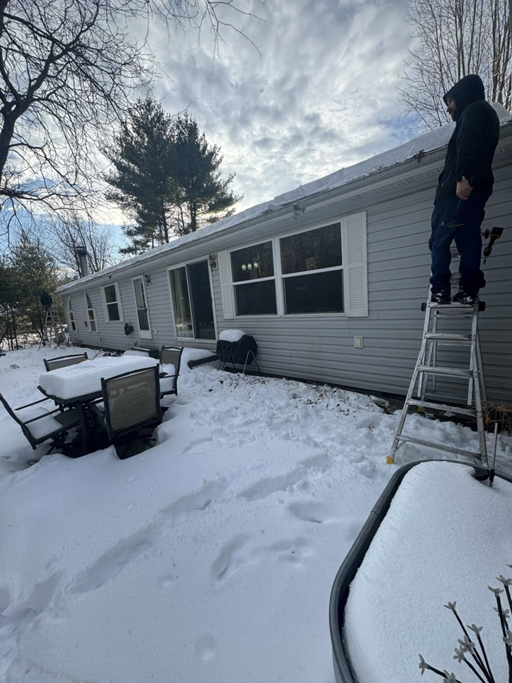 A handyman on a ladder repairing the exterior of a house during winter for Timeless Exteriors Inc in Fort Wayne, IN
