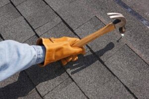 A handyman in a glove using a hammer to repair roof shingles for Spartan Roofing LLC in St. Louis, MO