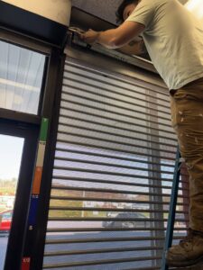 A handyman on a ladder repairing a commercial security gate, performed by Byrd Property Restoration, LLC in Parkersburg, WV.