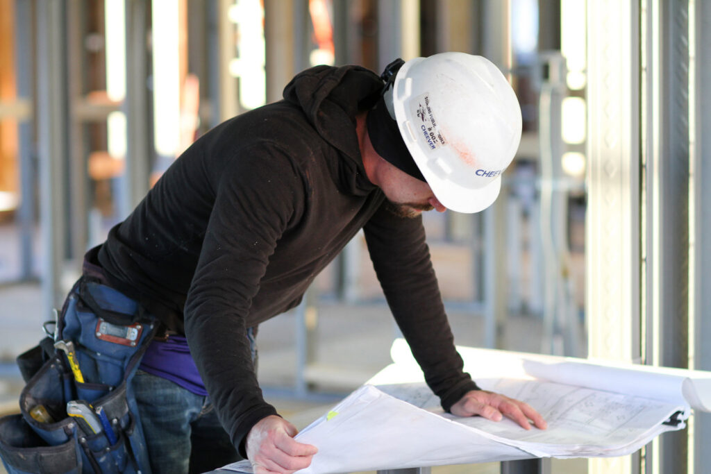 A handyman in a hard hat and tool belt reviewing blueprints at a construction site for Cheever Builders in Grand Rapids, MI.