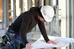 A handyman in a hard hat and tool belt reviewing blueprints at a construction site for Cheever Builders in Grand Rapids, MI.
