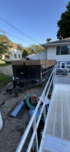A handyman performing roof repair with a dump trailer on site for debris removal by CRT Dump Trailer Rentals in Prior Lake, MN.