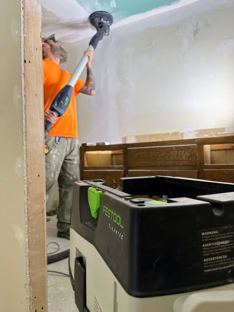 A handyman from Holaway Handyman sanding a ceiling during a drywall finishing job in Fayetteville, AR.
