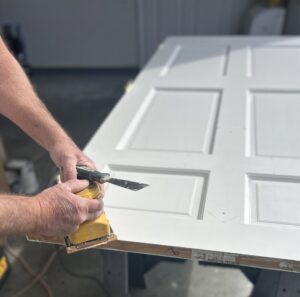 A handyman's hands sanding a white door in preparation for painting, a service offered by Randy Overacre Painting Company in Virginia Beach, VA.