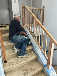 A handyman sanding a wooden staircase railing during a renovation project by Lambert's Residential Painting And More LLC in Fort Wayne, IN.