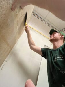 A handyman from Forever Young Handyman Services in Boise, ID, actively scraping wallpaper off a wall.