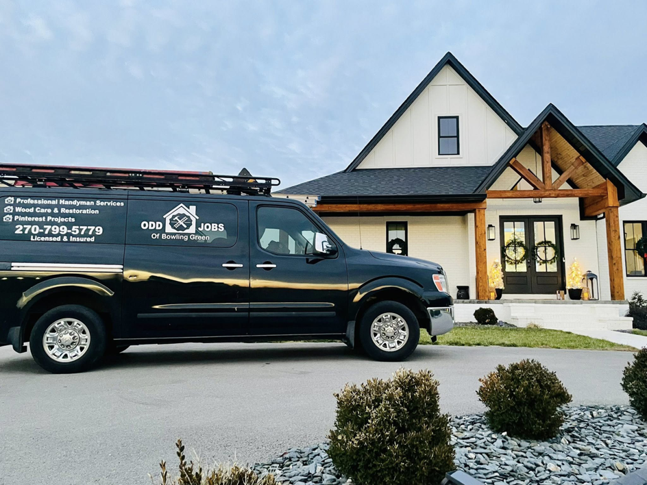 A black handyman service van from Odd Jobs of Bowling Green parked in front of a modern house in Bowling Green, KY, ready for a job.