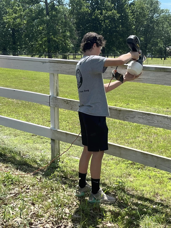 A handyman using a paint sprayer to paint a fence for S&S Handyman Services in Reno, NV