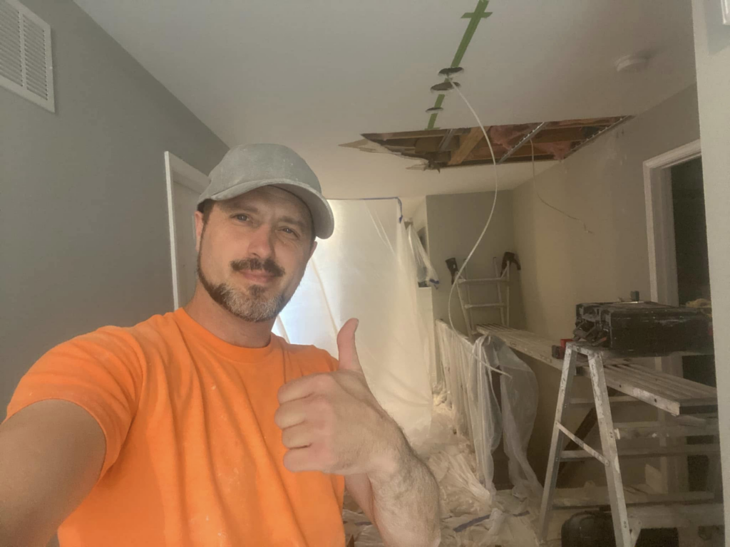 A handyman giving a thumbs-up on a ceiling repair job site for Walrus Rock Construction LLC in Pacific, MO.