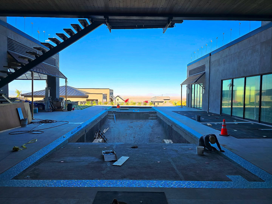 A handyman installing blue mosaic tiles on a pool border for Premier Paradise, Inc. in Gilbert, AZ.