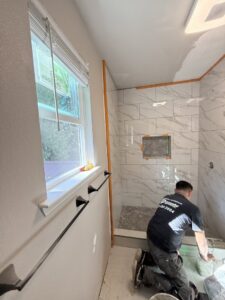 A handyman from JP. Remodel Service LLC tiling a shower wall in a bathroom in Everett, WA.