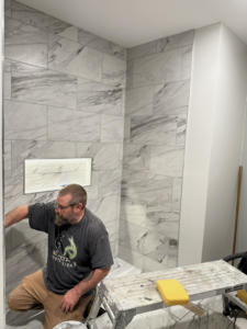 A handyman from Kizer Construction installing white marble-look tiles on a shower wall in Owensboro, KY.