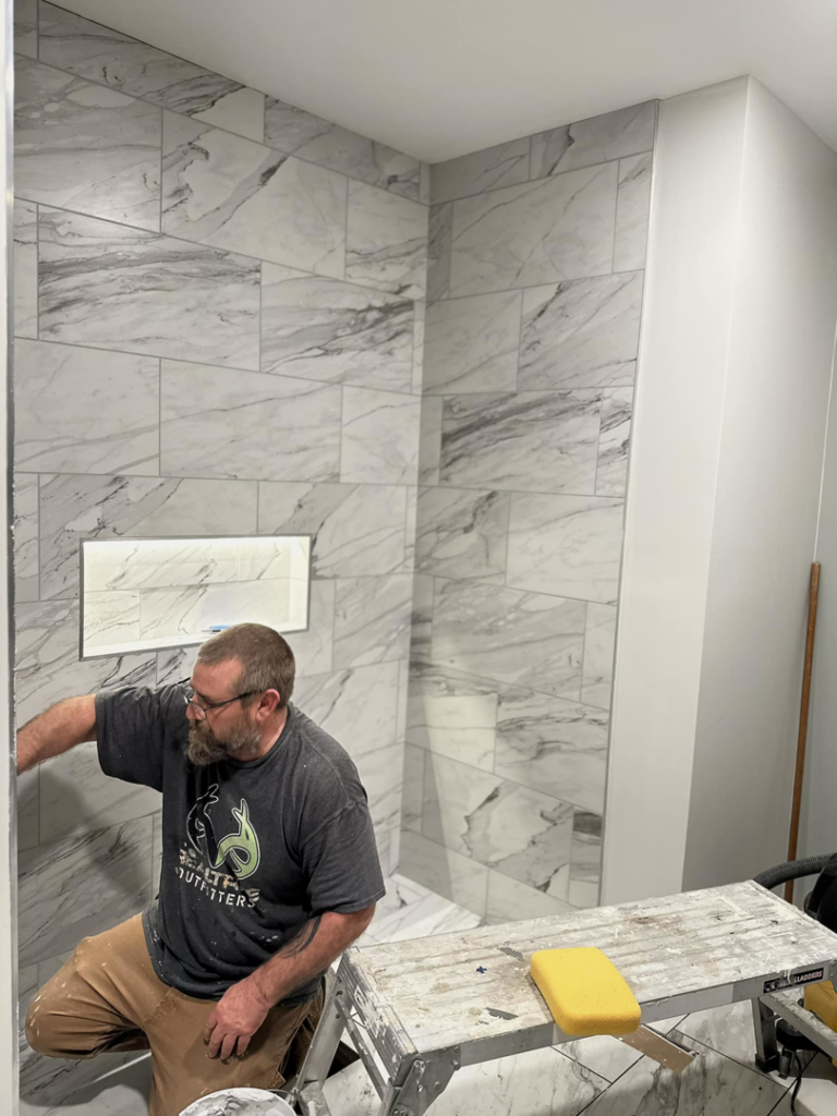 A handyman from Kizer Construction installing white marble-look tiles on a shower wall in Owensboro, KY.