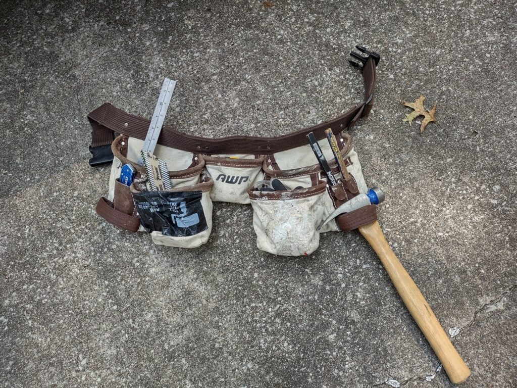 A handyman's tool belt with a hammer and other tools on concrete for Handyashby in Saint Joseph, MO.